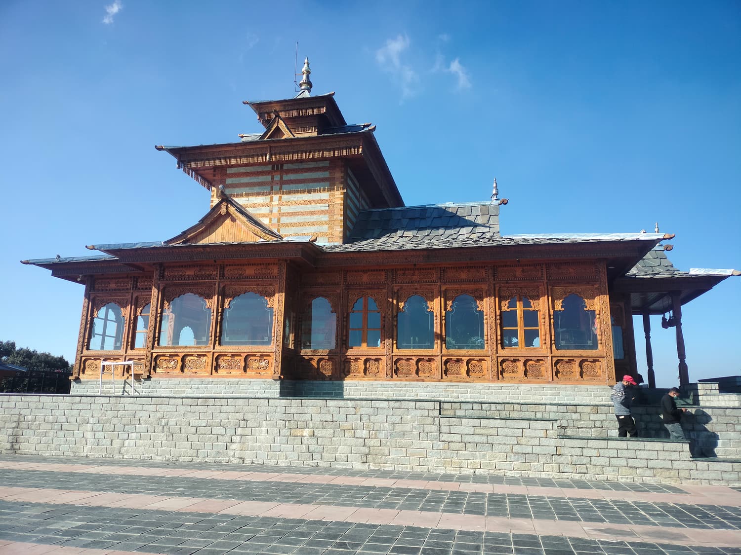 The carved-wood Tara Devi Temple on a stone platform under a blue sky
